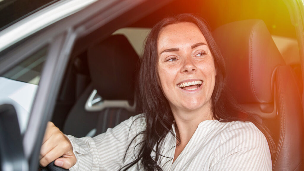 En glad kvinna sitter i förarsätet på en bil.